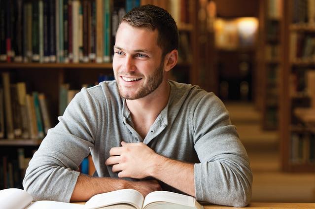 Un homme à la bibliothèque souriant avec des livres sur la table.