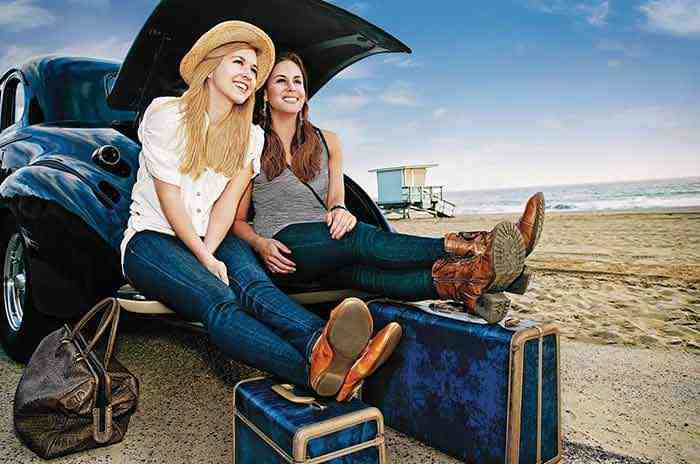 Zwei Frauen sitzen im Kofferraum ihres Autos am Strand und sind bereit ihre Ferien zu beginnen.